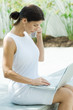 Woman using cell phone outdoors, looking down at laptop computer