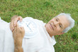 Senior man lying on grass, holding clock, smiling at camera