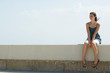 Young woman sitting on low wall outdoors, smiling, looking away