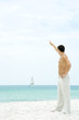 Photo: Man standing at the beach with arm raised, waving at sailboat in the distance, side view Man standing at the beach with arm raised, waving at sailboat in the distance, side view