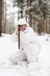 Soldier in white camouflage aiming with sniper rifle at winter f