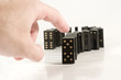 Human hand ready to push a row of black dominoes