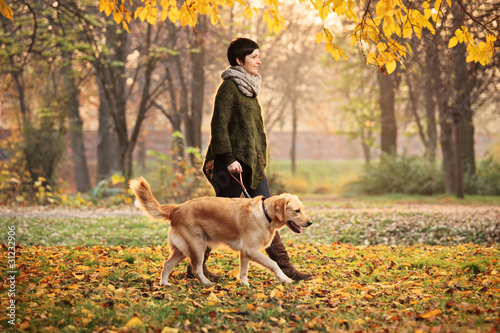 Photo: A girl and her dog walking in a park in autumn A girl and her dog walking in a park in autumn
