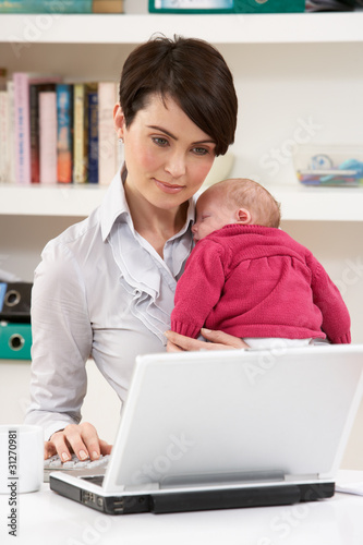 Photo: Woman With Newborn Baby Working From Home Using Laptop Woman With Newborn Baby Working From Home Using Laptop