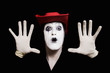 face and hands of mime with dark make-up in red hat