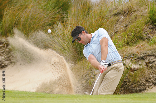 Foto: Golfer plays green side bunker shot Golfer plays green side bunker shot