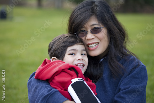 Photo: Beautiful asian mother holding her disabled son at park Beautiful asian mother holding her disabled son at park
