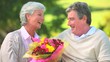 Video: Elderly couple holding a bunch of flowers while sitting on a bench Elderly couple holding a bunch of flowers while sitting on a bench