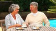 Mature couple having afternoon tea  by a swimming pool