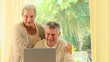 Elderly couple laughing at something on a laptop