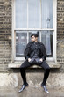 Photo: young fashionable man sitting on window-sill young fashionable man sitting on window-sill