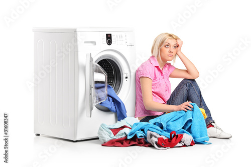 Photo: Thoughtful woman with clothes seated next to a washing machine Thoughtful woman with clothes seated next to a washing machine