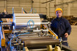 Factory worker processing roll of steel sheet.