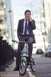 Foto: A businessman on his bicycle, talking on a mobile phone A businessman on his bicycle, talking on a mobile phone