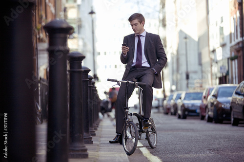 Photo: A businessman on his bicycle, looking at his mobile phone A businessman on his bicycle, looking at his mobile phone