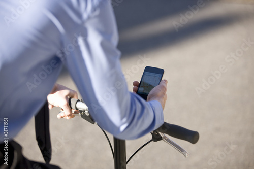 Foto: A businessman on his bicycle, looking at his mobile phone A businessman on his bicycle, looking at his mobile phone