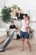 A Mother Trying To Vacuum While The Father Sits Around