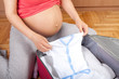 Pregnant woman packing baby clothing insuitcase