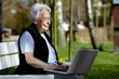 Nette alte Dame mit Laptop auf Bank 34