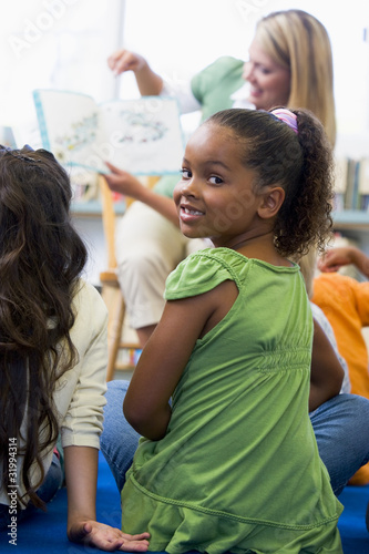 Photo: Kindergarten teacher reading to children in library, girl lookin Kindergarten teacher reading to children in library, girl lookin