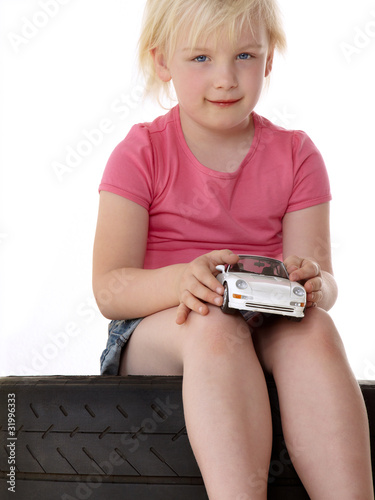 Foto: Blond girl sitting on a tyre and playing with a toy car Blond girl sitting on a tyre and playing with a toy car
