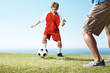 Small boy playing a soccer game with a man at ground