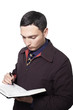 man in dark jacket and tie looking down and writing in planner