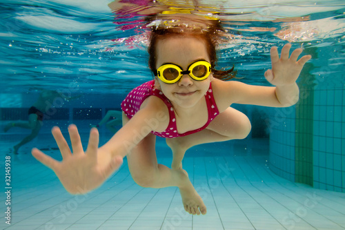 Photo: The girl smiles, swimming under water in the pool The girl smiles, swimming under water in the pool