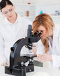 Blond-haired scientist looking through a microscope with her ass