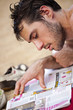 homme lit un magazine sur le sable en vacances