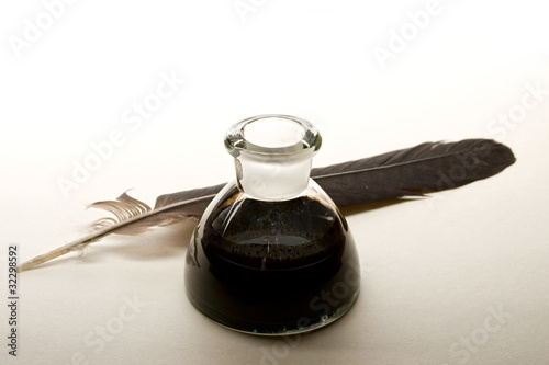 Photo: Feather and ink bottle isolated on paper background Feather and ink bottle isolated on paper background