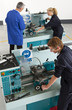 Teacher talking to students using lathe in vocational school