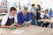 Teacher watching student using soldering iron in vocational school