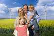 Photo: Happy family standing together in blooming field with wind turbines in background Happy family standing together in blooming field with wind turbines in background