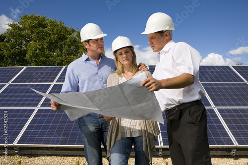 Foto: Technicians reviewing blueprints together near large solar panels Technicians reviewing blueprints together near large solar panels