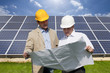 Technicians holding blueprints talking near large solar panels