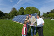 Technician holding blueprints talking to family near large solar panels