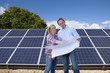 Technicians holding blueprints talking near large solar panels