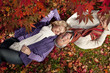 Smiling senior couple laying on ground underneath red autumn leaves
