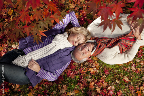 Photo: Smiling senior couple laying on ground underneath red autumn leaves Smiling senior couple laying on ground underneath red autumn leaves