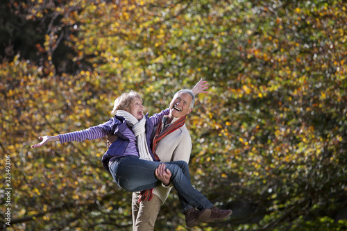 Photo: Laughing senior man carrying wife in autumn park Laughing senior man carrying wife in autumn park