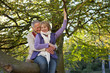 Smiling senior couple sitting on large tree branch