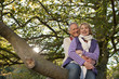 Smiling senior couple sitting on large tree branch