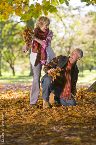 Foto: Playful senior couple throwing autumn leaves at one another Playful senior couple throwing autumn leaves at one another