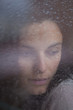 Traurige Frau hinter Fenster mit Regentropfen