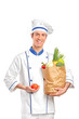 Smiling chef holding a tomato and paper bag full with vegetables Smiling chef holding a tomato and paper bag full with vegetables