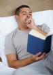 Young man yawning while reading book
