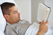 Young guy reading book while lying on bed