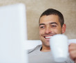 Photo: Happy young man sitting in front of laptop and having tea Happy young man sitting in front of laptop and having tea