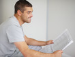 Young guy reading newspaper while looking away